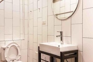 A bathroom with white tiled walls, a white sink with a mirror above it, and a toilet. - Oon Poshtel X Cafe (Chiang Mai)