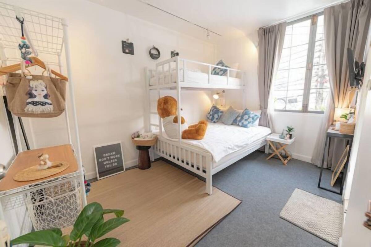 Um quarto aconchegante com uma cama de solteiro e beliche, uma mesinha de cabeceira pequena, uma bolsa pendurada e um cartaz motivacional.