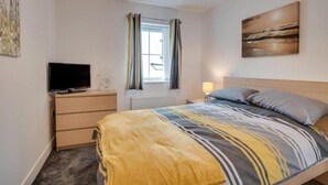 Una camera da letto con un letto, una televisione su un comodino, una finestra con tende e un quadro appeso al muro.