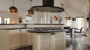 A modern kitchen with a central island, pendant lighting, and a large stove. - Wellness Villa With Sauna, spa Near Beach (Ouddorp)