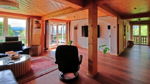A spacious living area with wooden beams, a sofa, a coffee table, and a view of the outdoors. - Holiday Home Scharzwald (Feldberg)