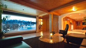A modern living room with a large TV screen displaying a cityscape, wooden ceiling, and comfortable seating. - Holiday Home Scharzwald (Feldberg)