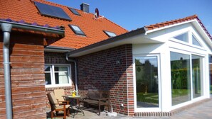 A house with a brick exterior, a tiled roof, and a covered patio area with a table and chairs. - Holiday Apartment Gerdes (Wangerland)