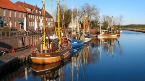 A calm canal with several traditional boats docked, a brick building with a red roof, and a clear blue sky. - Holiday Apartment Gerdes (Wangerland)