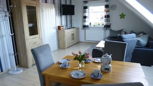 A dining area with a wooden table set for two, a television mounted on the wall, and a cozy seating area with a sofa and armchairs. - Holiday Apartment Gerdes (Wangerland)