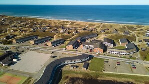 An aerial view of a coastal area with buildings, a tennis court, and a parking lot. - 8 Person Holiday Park Home in Ringkobing (Ringkobing)