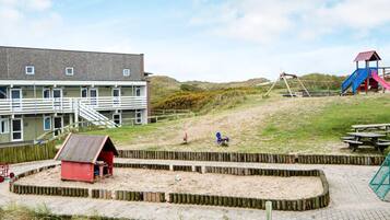 A beachside building with a sandy play area, a red structure, and a playground with slides.