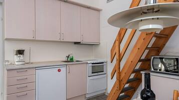 A kitchen with pink cabinets, a white refrigerator, a stove, and a microwave. There is a wooden staircase and a hanging light fixture.