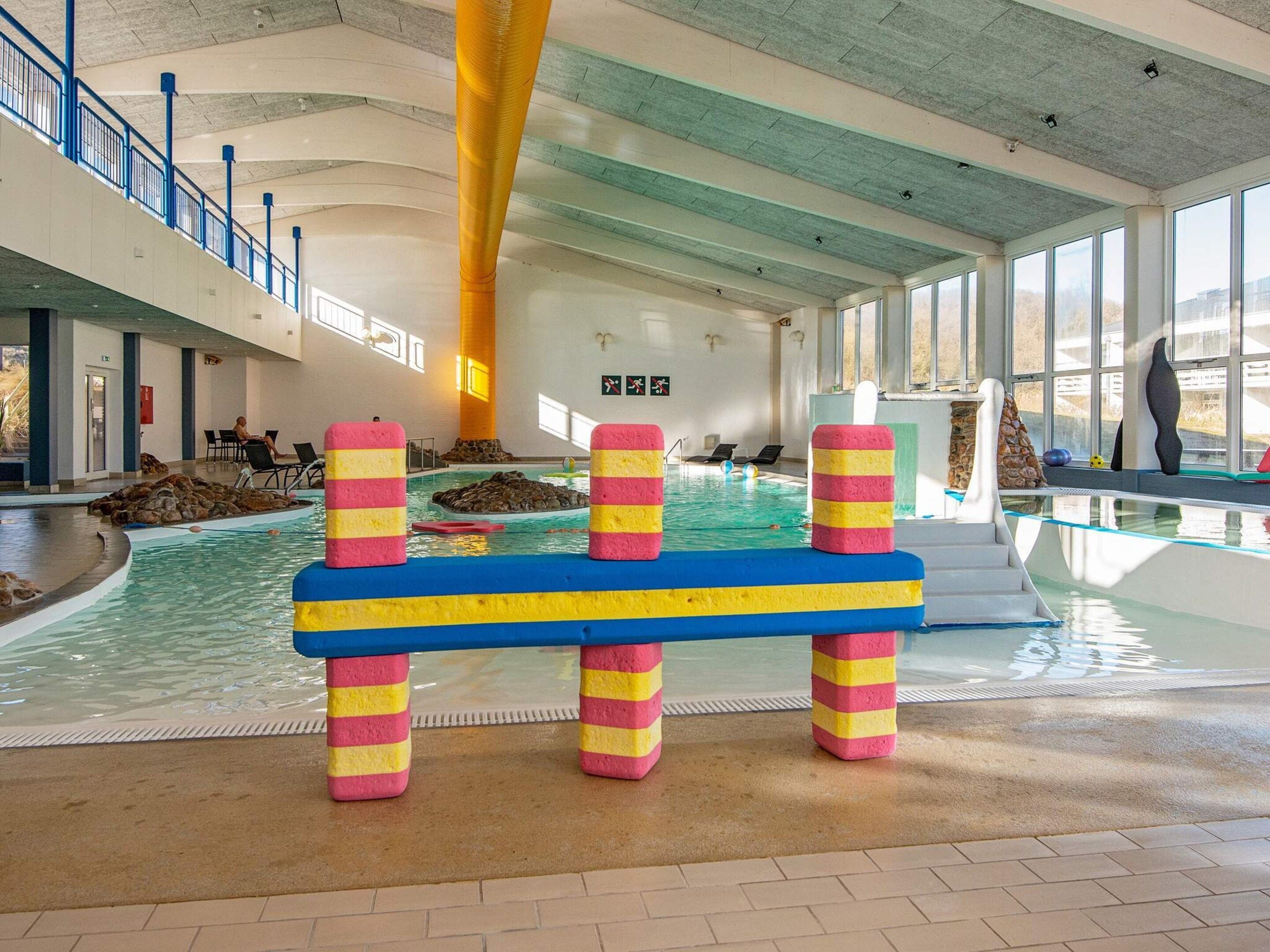An indoor swimming pool with colorful barriers, a stone wall, and a view of the outside through large windows.
