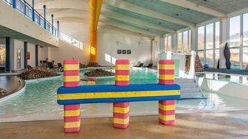 An indoor swimming pool with colorful barriers, a stone wall, and a view of the outside through large windows.