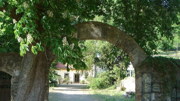 Un arco de piedra que da acceso a un edificio con tejado de tejas rojas.
