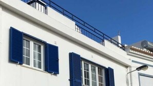 Un edificio blanco con contraventanas azules, un balcón y una banca en el exterior.