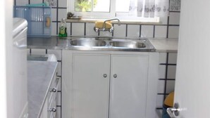Una cocina con armarios blancos, un lavamanos doble y una ventana con cortina.