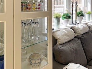 Ett rum med ett glasskåp där olika typer av glasvaror visas och en soffa med kuddar.