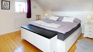 Ein Schlafzimmer mit einem Bett, einer Bank, einem Nachttisch und einem Fenster mit Vorhängen.
