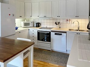 Ett kompakt kök med vita skåp, en mikrovågsugn, en ugn och en diskmaskin.