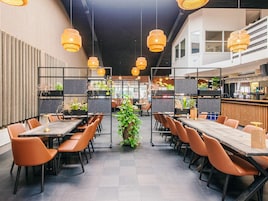 A modern restaurant with high tables, orange chairs, and hanging wicker lamps.