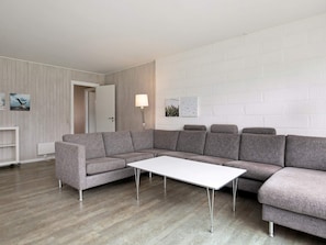 Un salon moderne avec un canapé d’angle gris, une table basse blanche et une lampe.