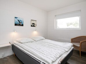 Une chambre à coucher avec un lit, deux lampes fixées au mur, une fenêtre et deux tableaux encadrés.