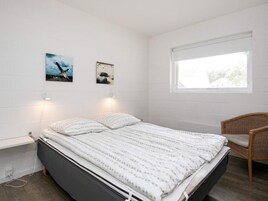 A bedroom with a bed, two wall-mounted lamps, a window, and two framed pictures.