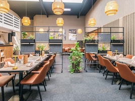 Un espace de restauration moderne avec de longues tables, des chaises marron et des lampes en osier suspendues.