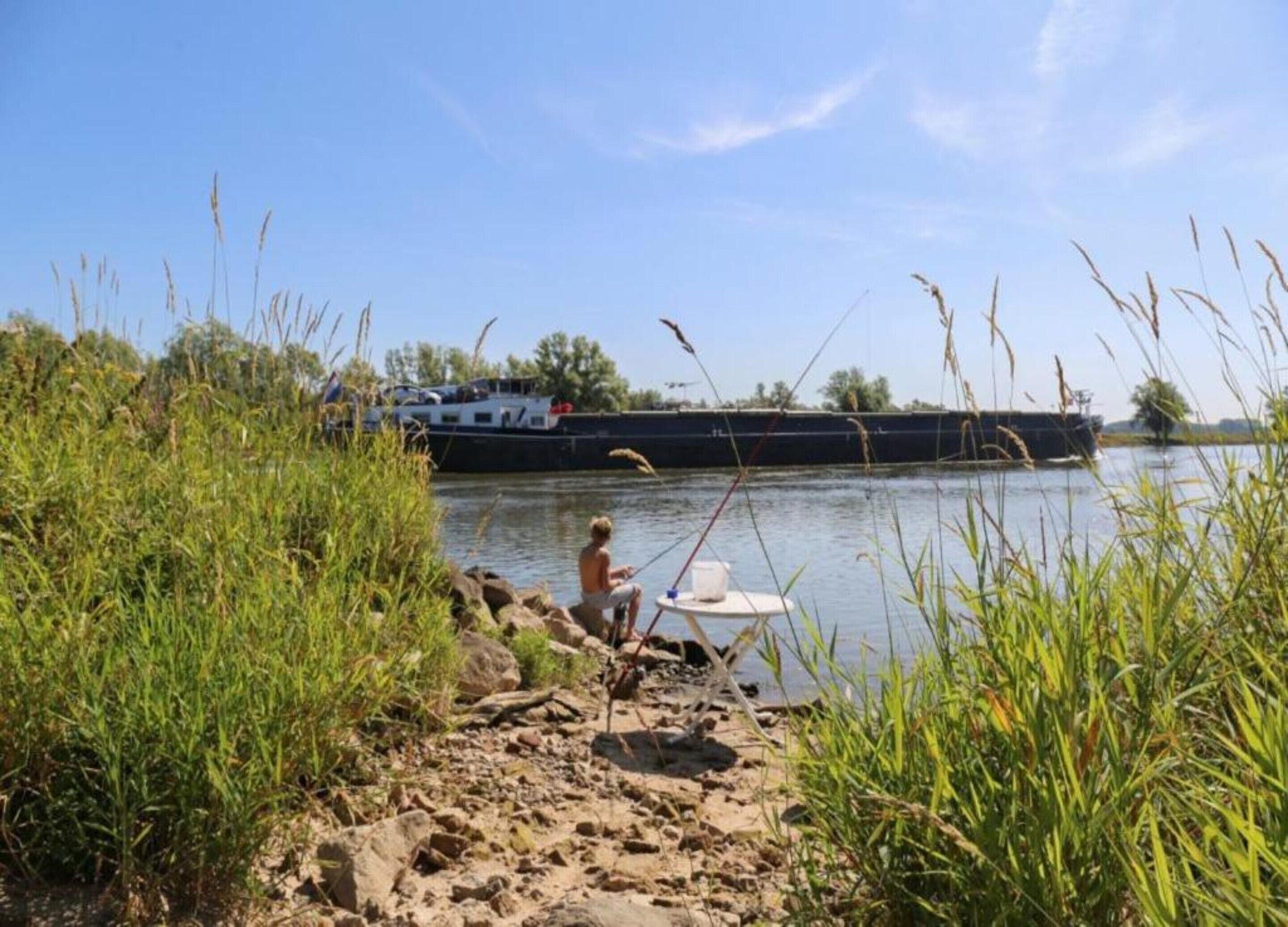 A person fishing by a river with a boat in the background.