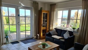 A living room with a dark-colored sofa, a wooden coffee table, and a view of a green landscape through large sliding glass doors. - "moseltor" Comfortable Holiday Residence (Monzelfeld)