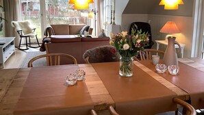 Un comedor con una mesa de madera, sillas y un florero. Hay dos lámparas colgantes sobre la mesa.