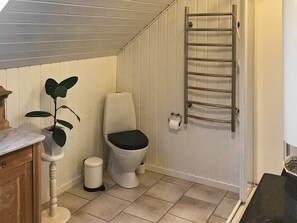 Ein kleines Badezimmer mit Toilette, Mülleimer, Handtuchhalter und einer Topfpflanze.