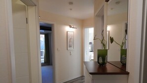 A hallway with a wooden floor, a white door, and a mirror on a dresser. - 11 Bohler Brise Modern Retreat (St. Peter-Ording)