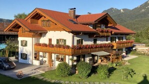 A two-story chalet with a balcony, surrounded by a well-maintained garden and mountains in the background. - No. 2 - Country House Geierstanger (Wallgau)