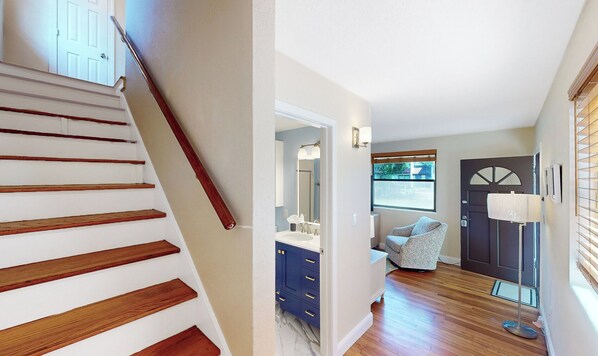 Una escalera de madera con barandilla que conduce a un baño con lavamanos, espejo y muebles azules.