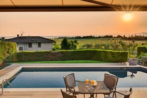 Una piscina con dos sillas y una mesa, una casa al fondo y una vista despejada del paisaje.