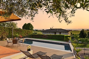 A swimming pool with lounge chairs, a table with chairs, and a view of the countryside.