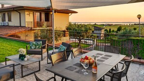 An outdoor patio with a table set for dining, surrounded by chairs, and a view of a house and landscape. - Regarda - Villa Celebrity with private pool and stunning lake view (Lazise)