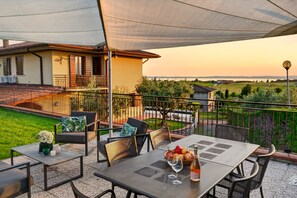 Une terrasse extérieure avec une table dressée pour le repas, entourée de chaises, et offrant une vue sur une maison et le paysage environnant.