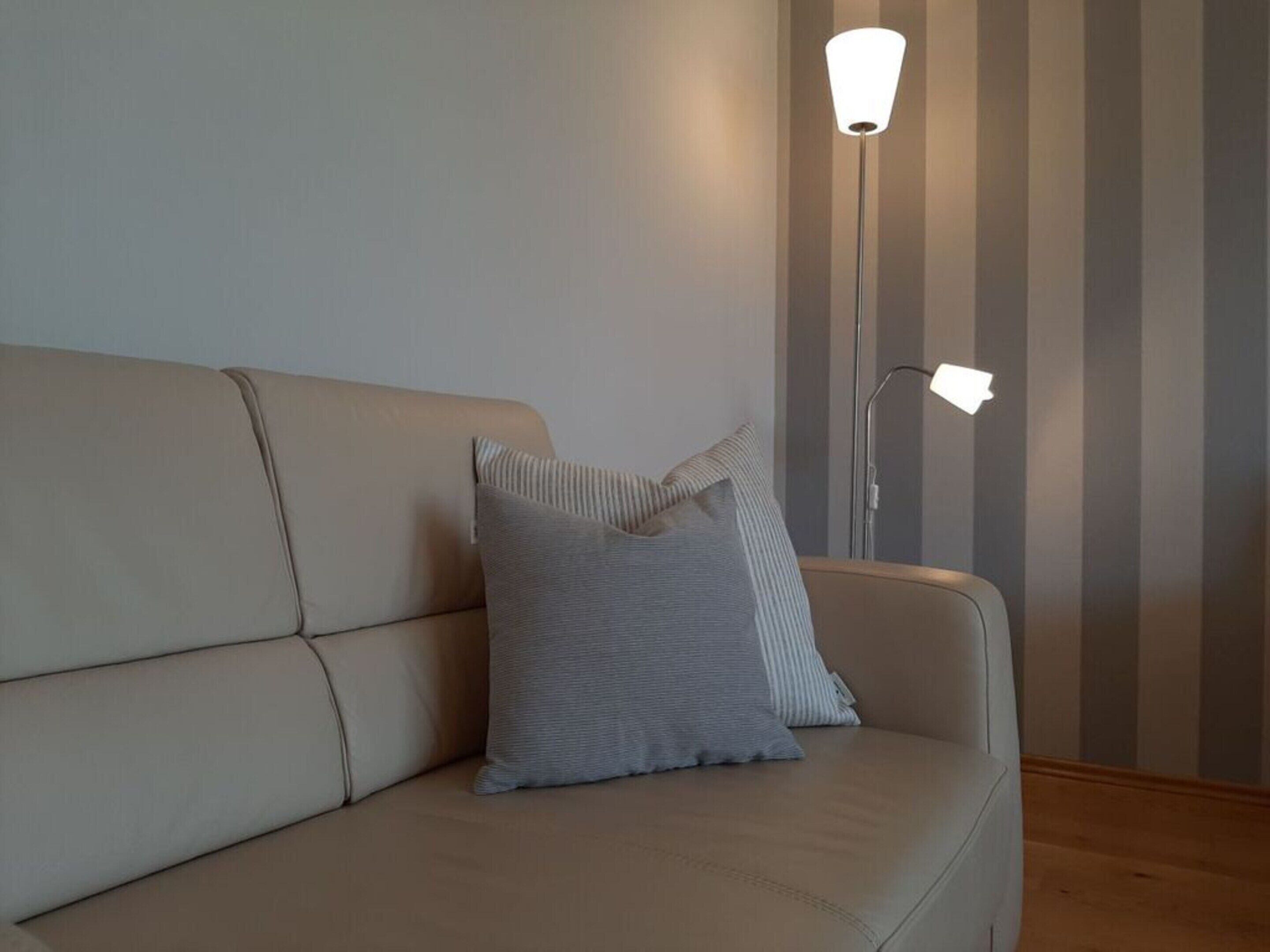 A beige sofa with a striped pillow, a floor lamp, and a striped wall.