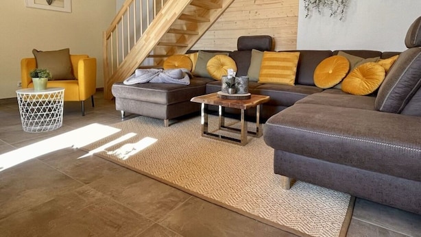 Un salon moderne avec un escalier en bois, un ensemble de canapés et un élément décoratif mural.