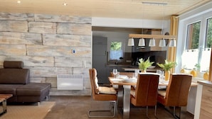Un intérieur moderne avec un mur en pierre, un coin repas avec une table et des chaises en bois, et une cuisine en arrière-plan.