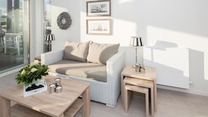 Una sala de estar moderna con sofá, mesa de centro y mesita auxiliar, con vistas a través de un ventanal.