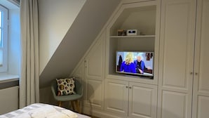 Une chambre avec un téléviseur fixé au plafond en pente, une chaise avec un coussin en forme de coquillage et un lit avec une literie à motifs.