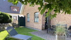 Un espace patio aménagé avec un transat, des sièges d’extérieur et un pot de fleurs.