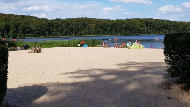 A beach with tents and people, a lake, and forested hills in the background. - Golf Idyll Holiday Apartment (Korswandt)