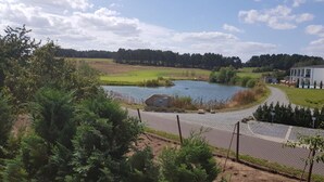 A lakeside view with a pathway leading to a building, surrounded by greenery and trees. - Golf Idyll Holiday Apartment (Korswandt)