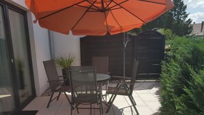 An outdoor patio with a table and chairs, an orange umbrella, and a potted plant. - Golf Idyll Holiday Apartment (Korswandt)