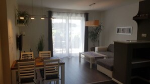 A modern living room with a sofa, a coffee table, and a dining area with a table and chairs. - Golf Idyll Holiday Apartment (Korswandt)