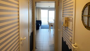 A hotel corridor with striped walls, a view to a balcony with a table and chairs, and a ship's wheel on the wall.