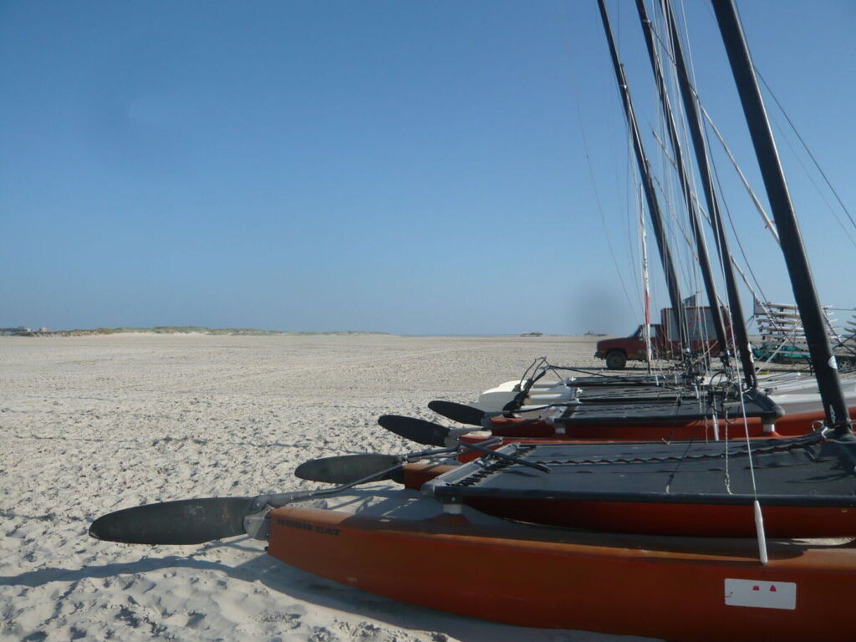 Una hilera de botes anaranjados en una playa arenosa bajo un cielo despejado.