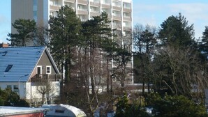 A multi-story building with balconies, surrounded by trees and a parked vehicle. - Holiday Apartment Beach View (St. Peter-Ording)