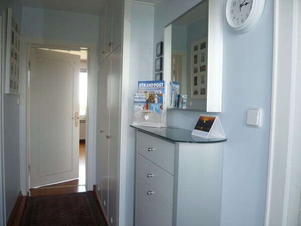A hallway with a glass-top desk, a clock, and a door leading to another room.